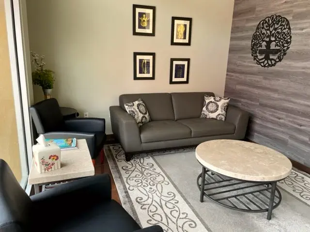 The Bernalillo waiting room: a grey sofa and chairs, a round stone table and a tree-of-life on a wood-plank wall