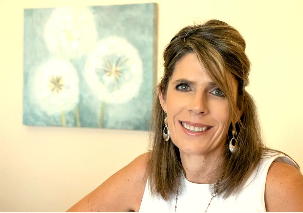 Dr. Tracy Marquez smiling in her office in front of a painting of white dandelions