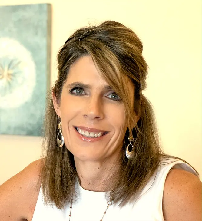 Dr. Tracy Marquez smiling, with long brown hair, drop earrings and a white sleeveless top