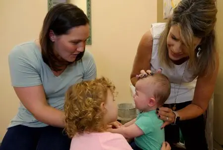 Dr. Marquez gently checking a baby’s neck while his mother and big sister hold him