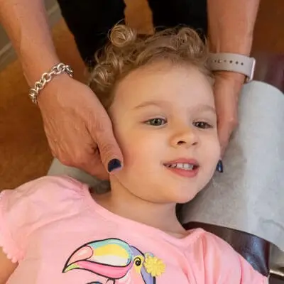 A curly-haired little girl in a pink toucan T-shirt smiling while Dr. Marquez checks her neck