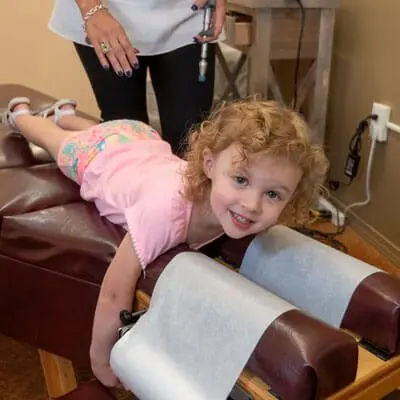 A smiling little girl lying on the adjusting table, chin on her hands