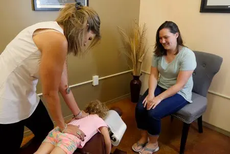 Dr. Marquez adjusting a little girl on the table while her mother watches from a chair