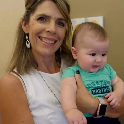 Dr. Marquez smiling and holding a baby boy in a green “Brother” T-shirt