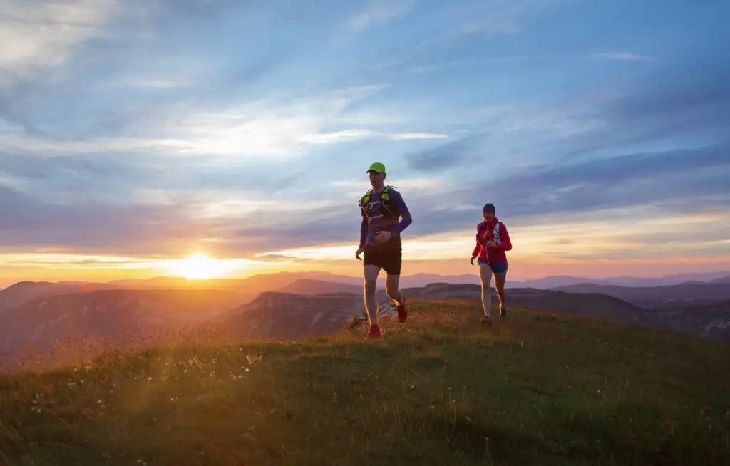 Two trail runners on a mountain ridge at sunset