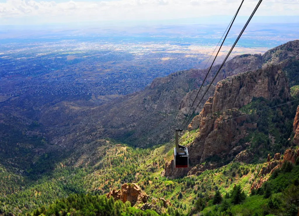 A Sandia Peak Tramway car climbing its cables above green canyons, Albuquerque spread out below