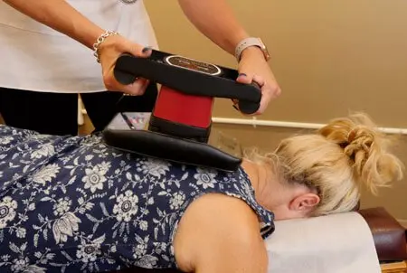 Dr. Marquez using a hand-held vibration massager on a patient’s upper back